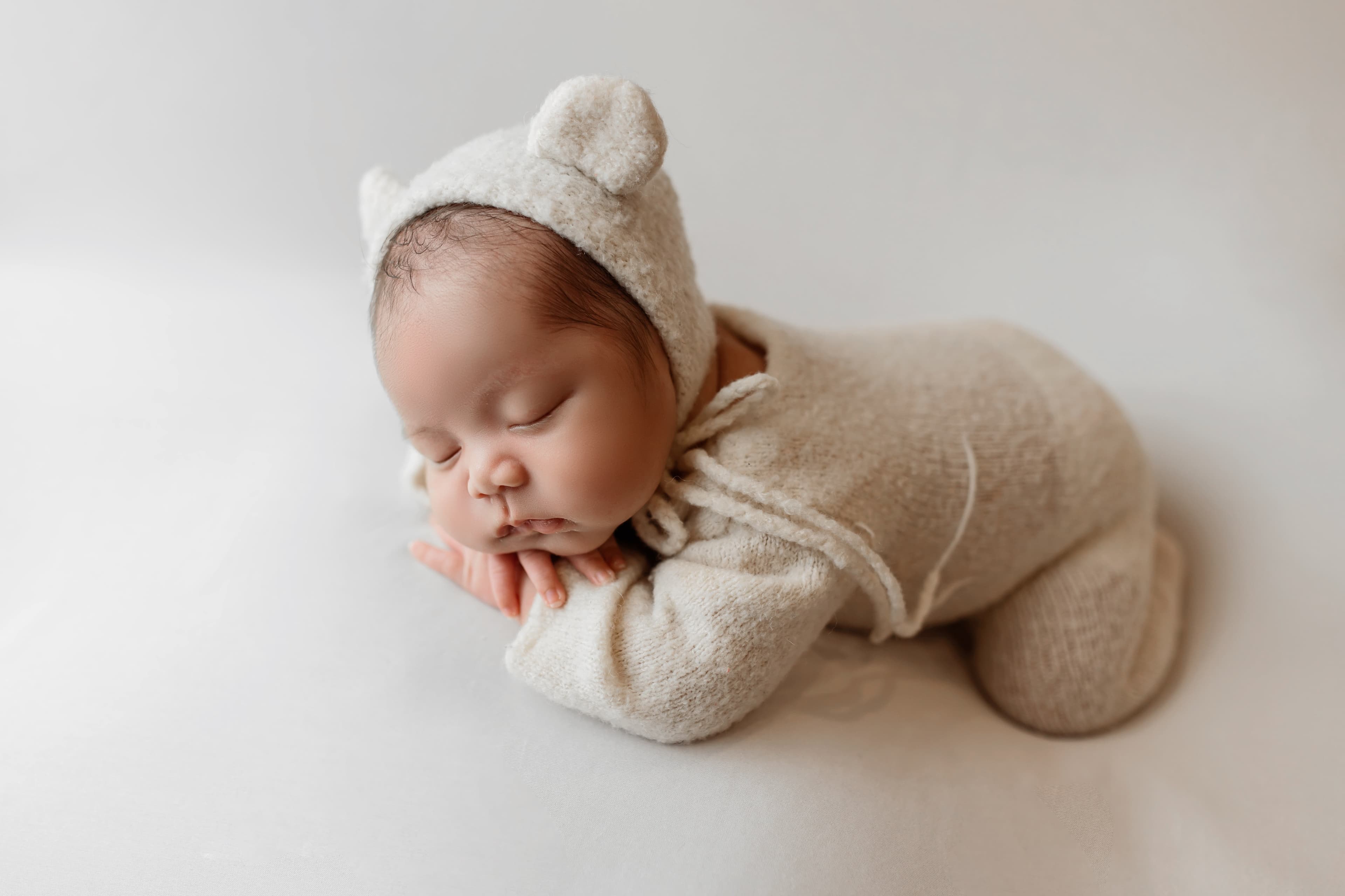 Newborn in cream knit outfit sleeping peacefully